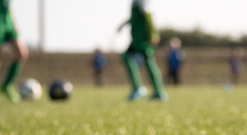 Konstgräs plan med fotbollsspelande ungdomar. Foto.