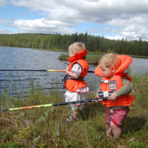 Två små barn i flytväst fiskar från stranden. Foto.