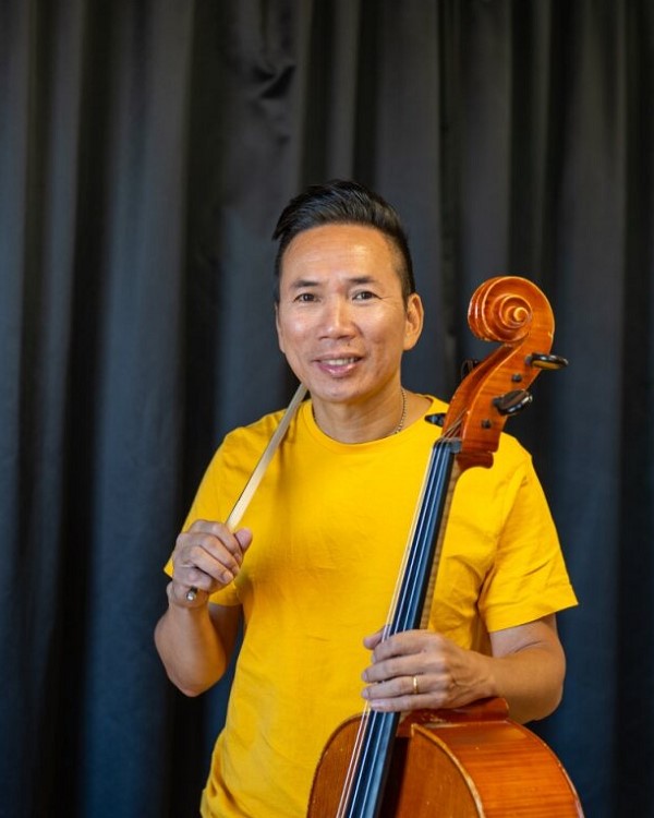 Man med mörkt hår håller i stränginstrument. Foto.
