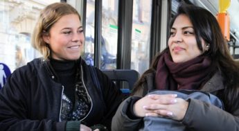 två glada, unga kvinnor sitter bredvid varandra i en buss