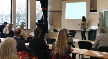 Personer som sitter i en föreläsningssal och tittar på en presentation.